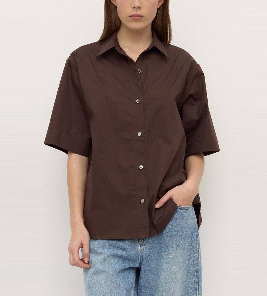 Person wearing a brown short-sleeve shirt and blue jeans against a white background