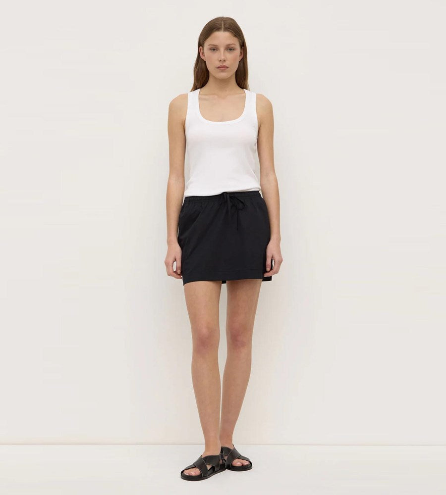 Woman wearing a white tank top and black skirt on a plain background