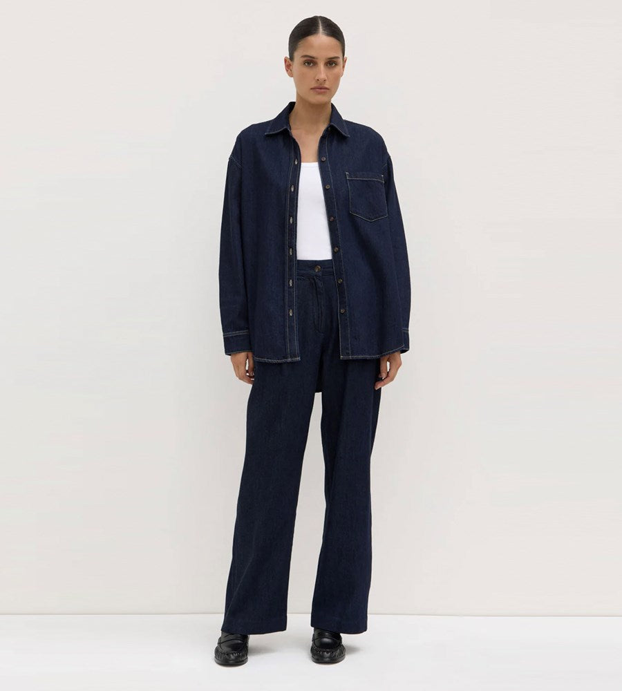 Person wearing a dark denim jacket and pants on a white background