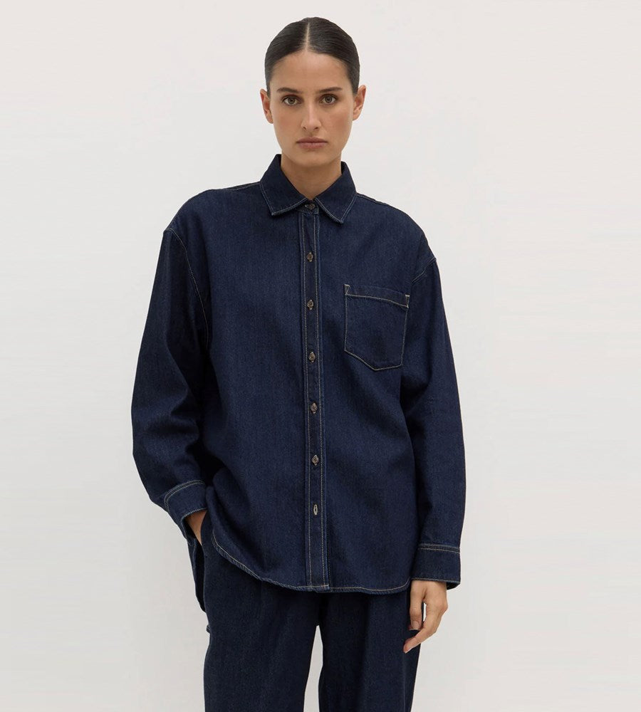 Person wearing a dark denim shirt and pants on a plain background
