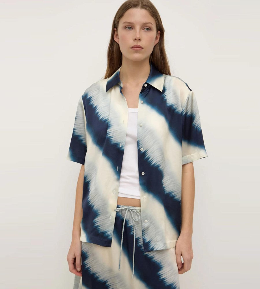 Woman wearing a tie-dye shirt over a white top on a plain background
