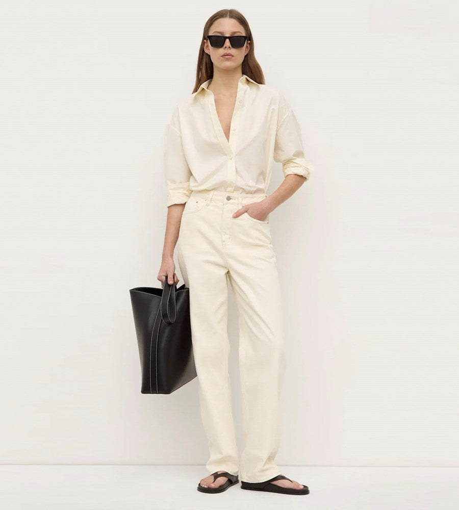 Woman in a cream outfit holding a black bag against a white background