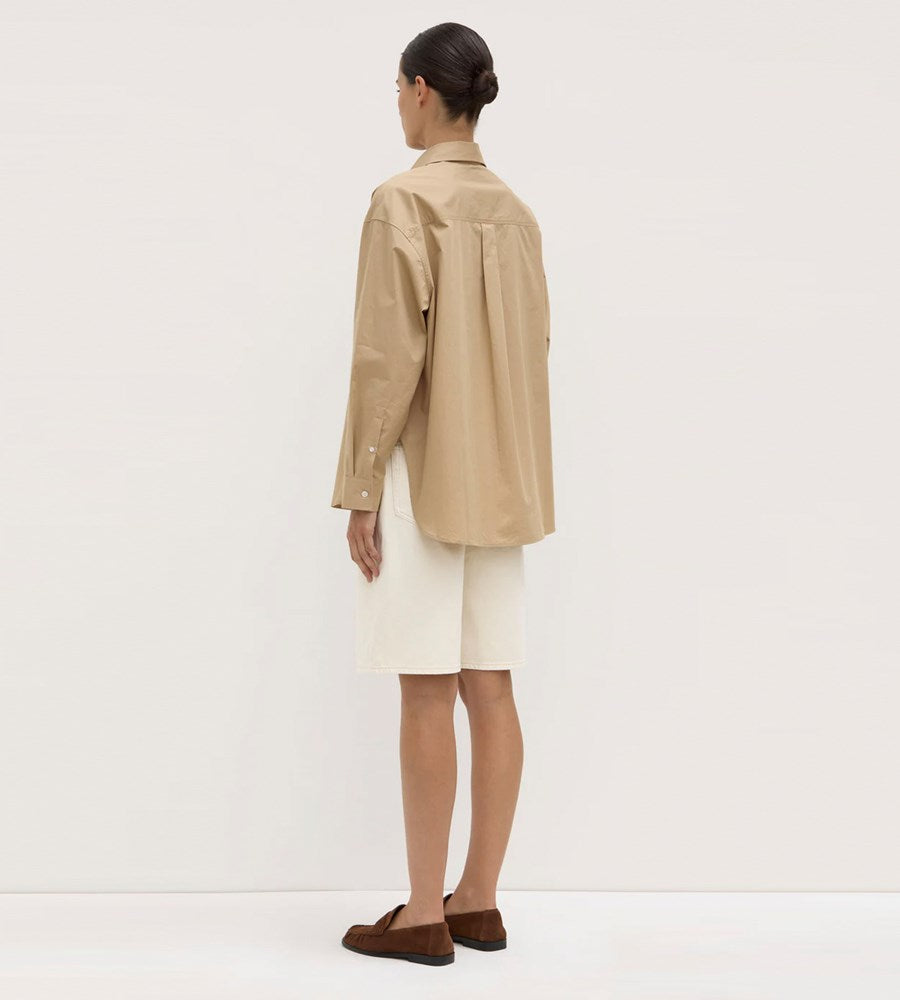 Person wearing a beige jacket and white skirt against a plain background