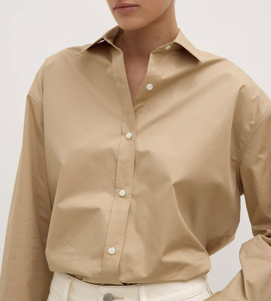 Beige button-up shirt worn by a person on a light gray background
