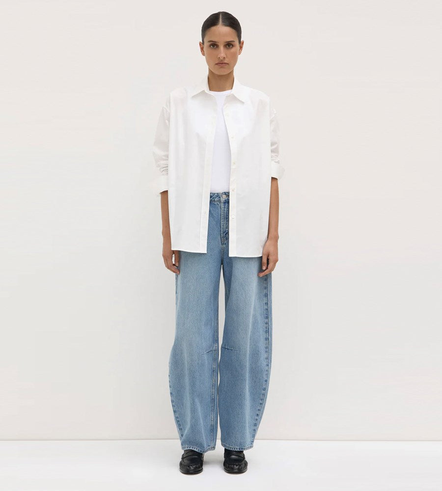 Person wearing a white shirt and light blue jeans on a plain background