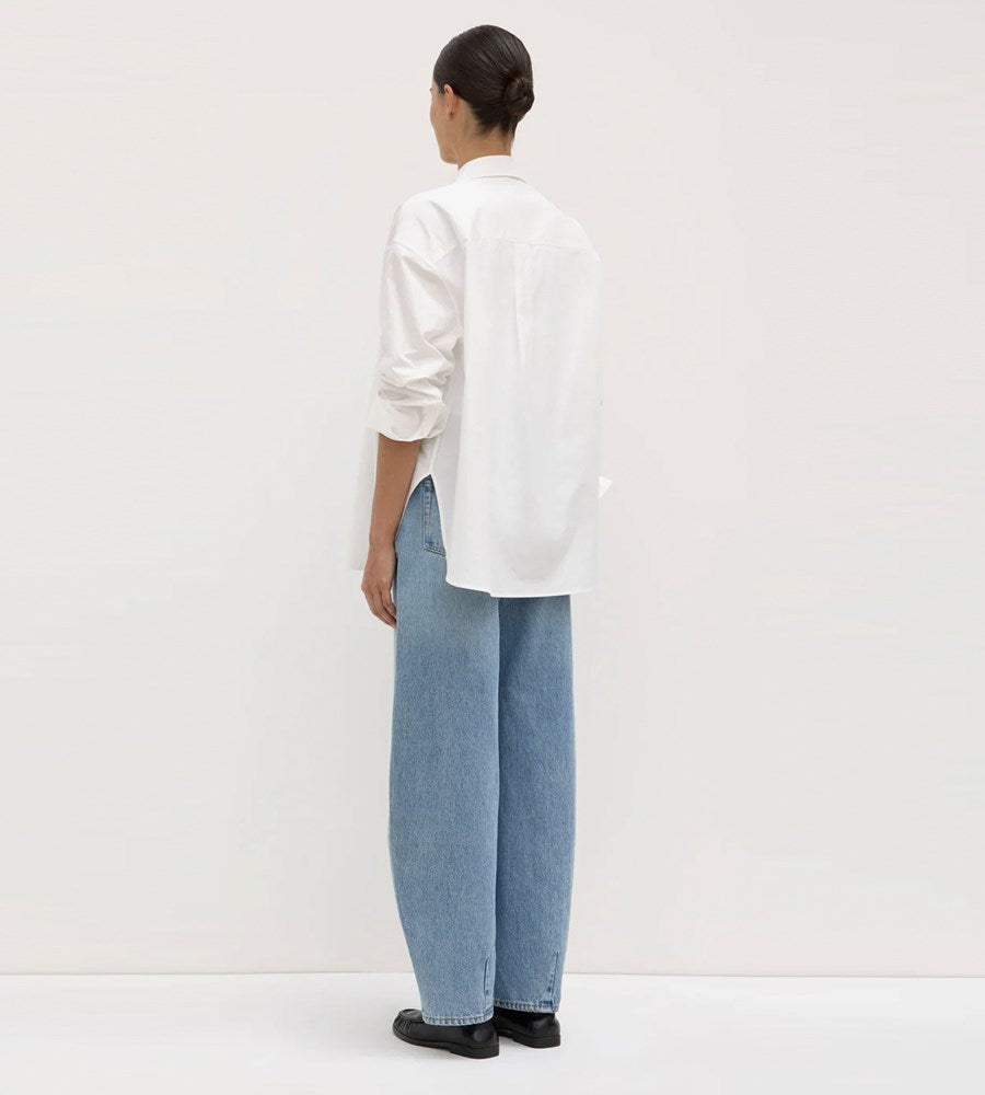 Person wearing a white shirt and light blue jeans against a plain background