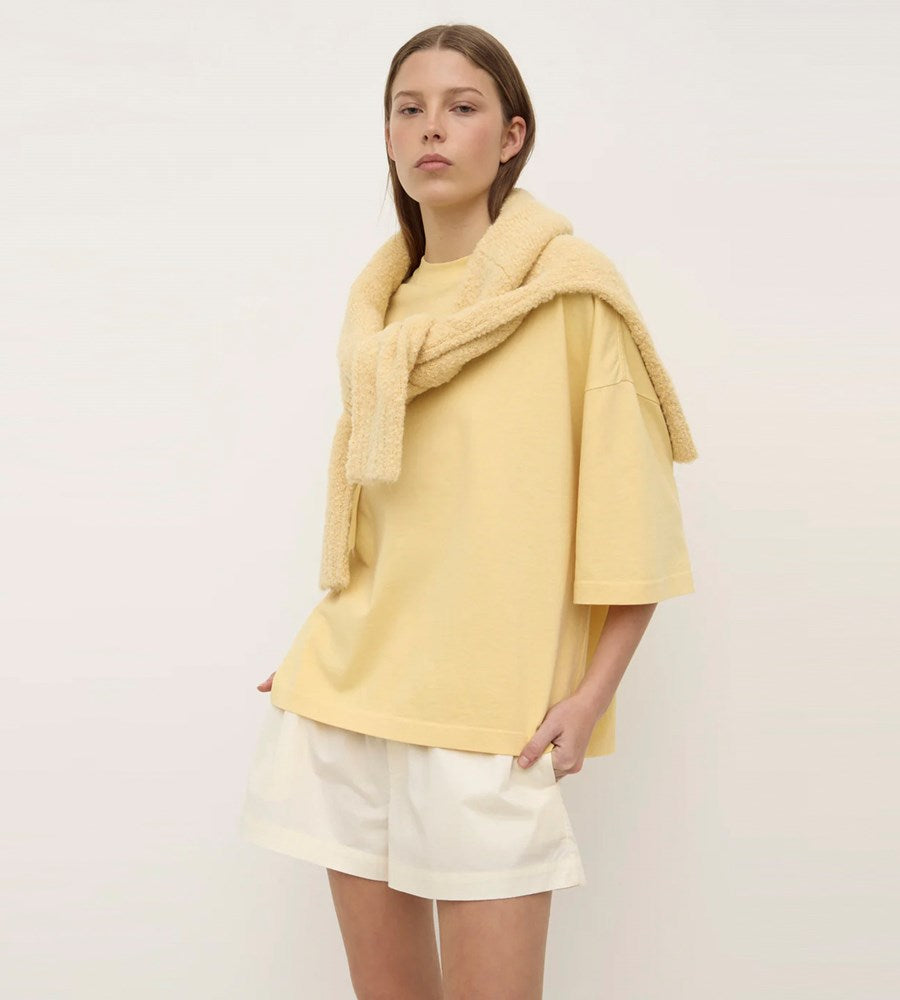 Woman wearing a yellow outfit with a scarf against a plain background