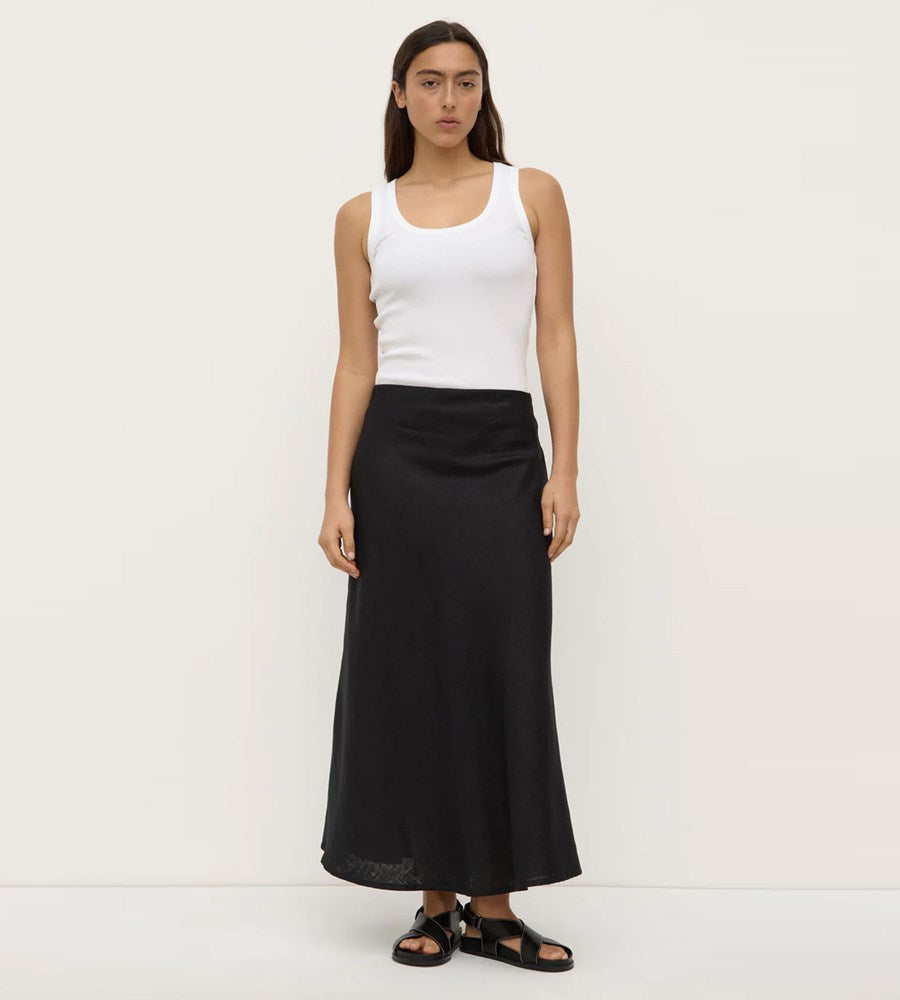 Woman wearing a white tank top and black long skirt on a white background