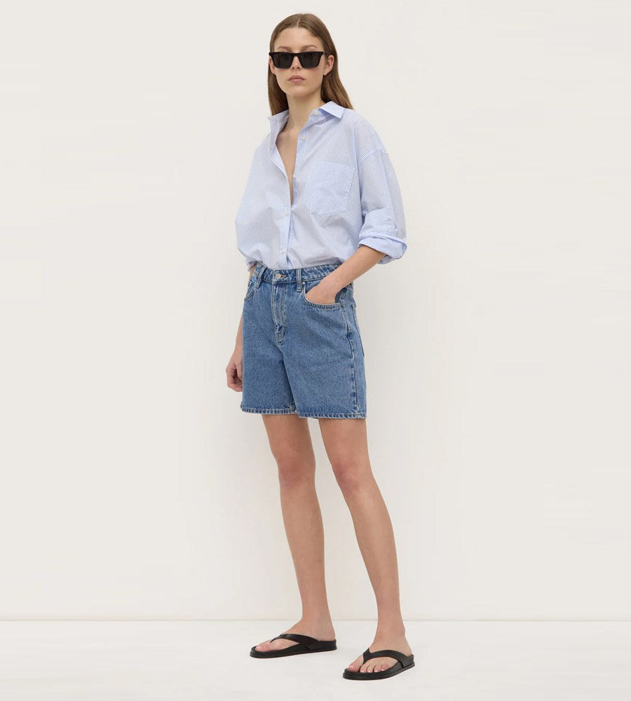 Woman wearing a light blue shirt and denim skirt against a white background