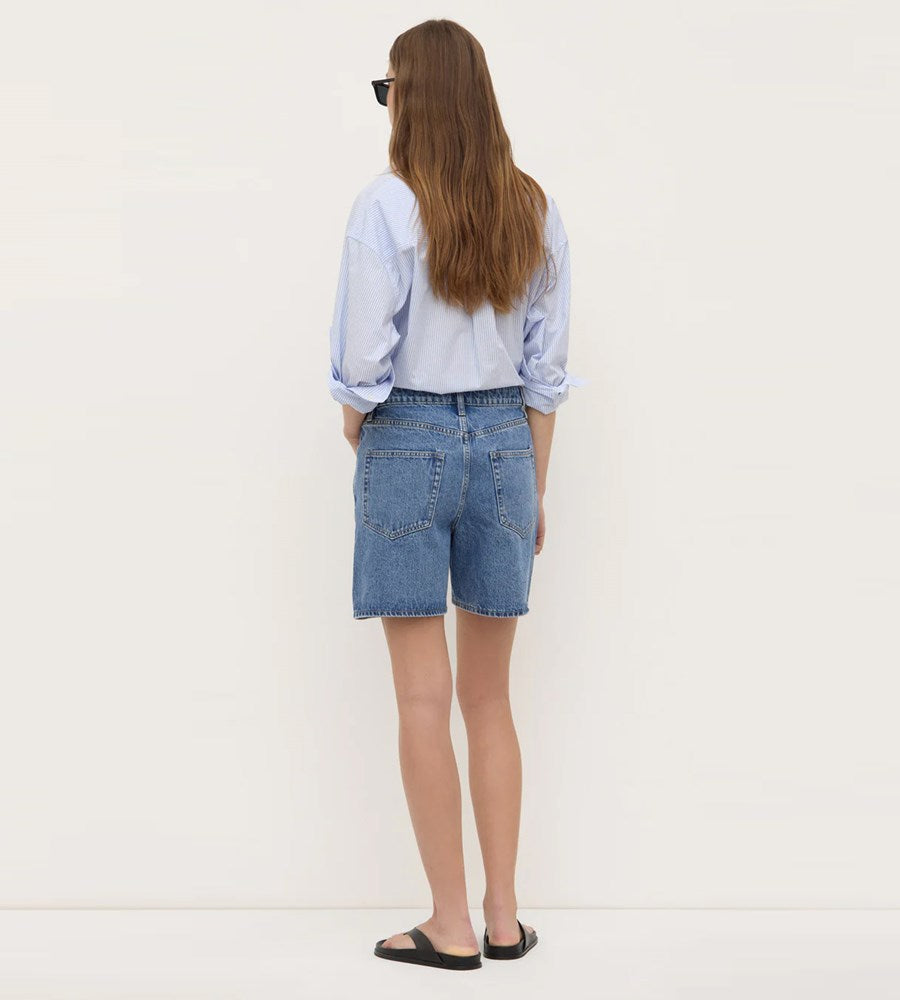 Person wearing a light blue shirt and denim shorts on a white background