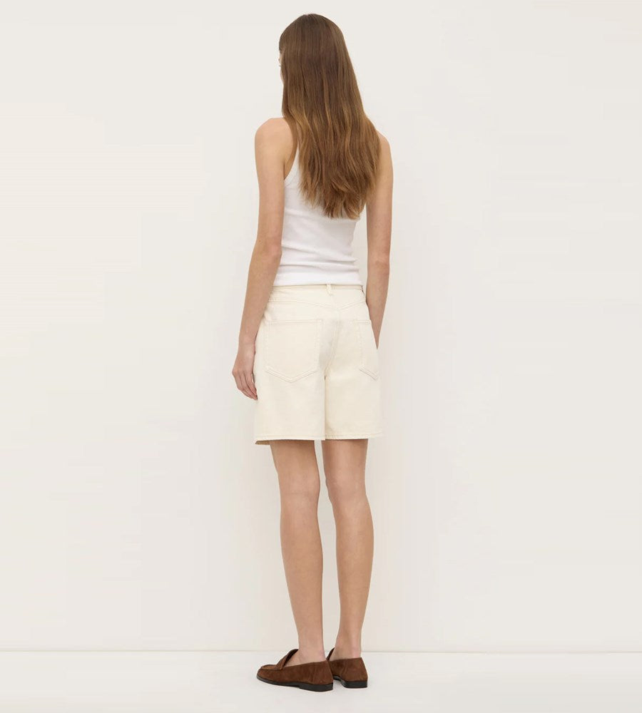 Woman wearing a white tank top and cream-colored skirt against a plain background