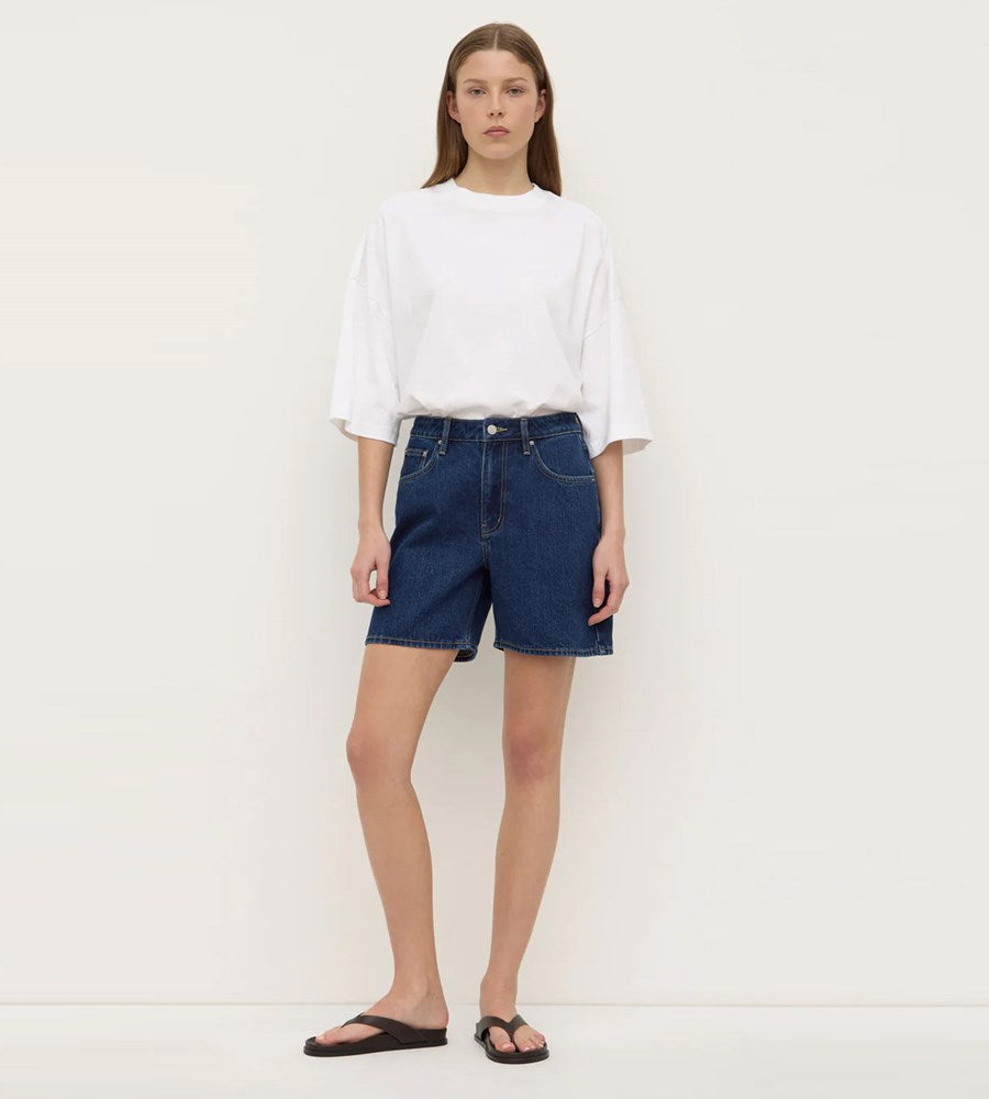 Person wearing a white t-shirt and blue denim shorts on a plain background