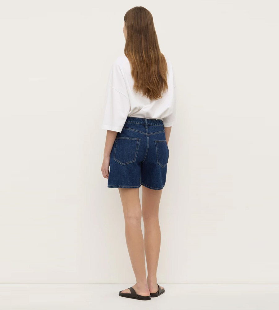 Person wearing blue denim shorts and a white shirt on a plain background