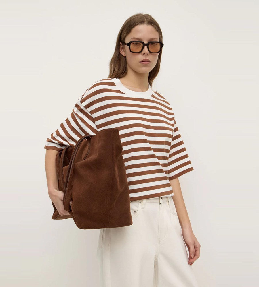 Woman wearing a brown and white striped shirt with a brown bag on a plain background