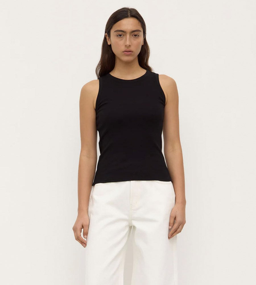 Woman wearing a black sleeveless top and white pants on a plain background