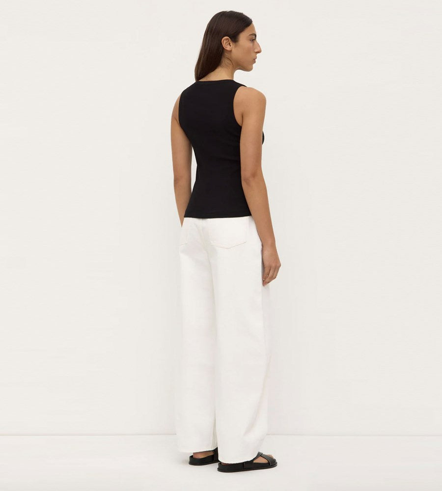 Woman wearing a black sleeveless top and white pants on a plain background