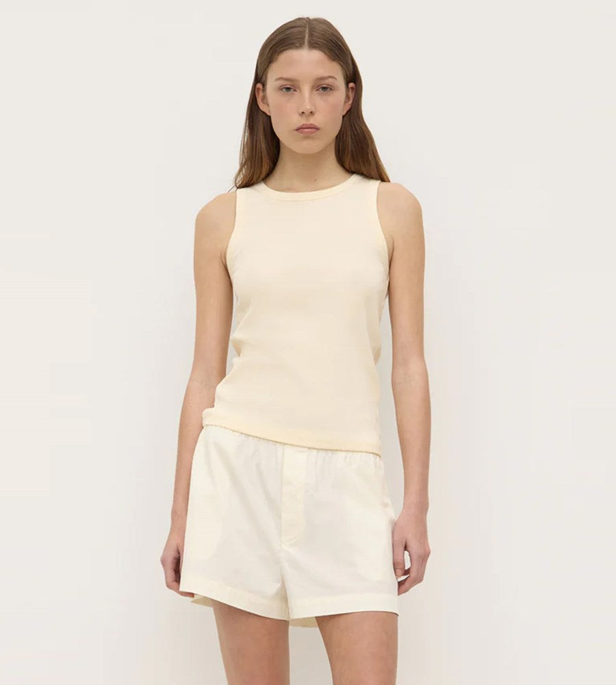Woman wearing a light yellow sleeveless top and shorts on a white background
