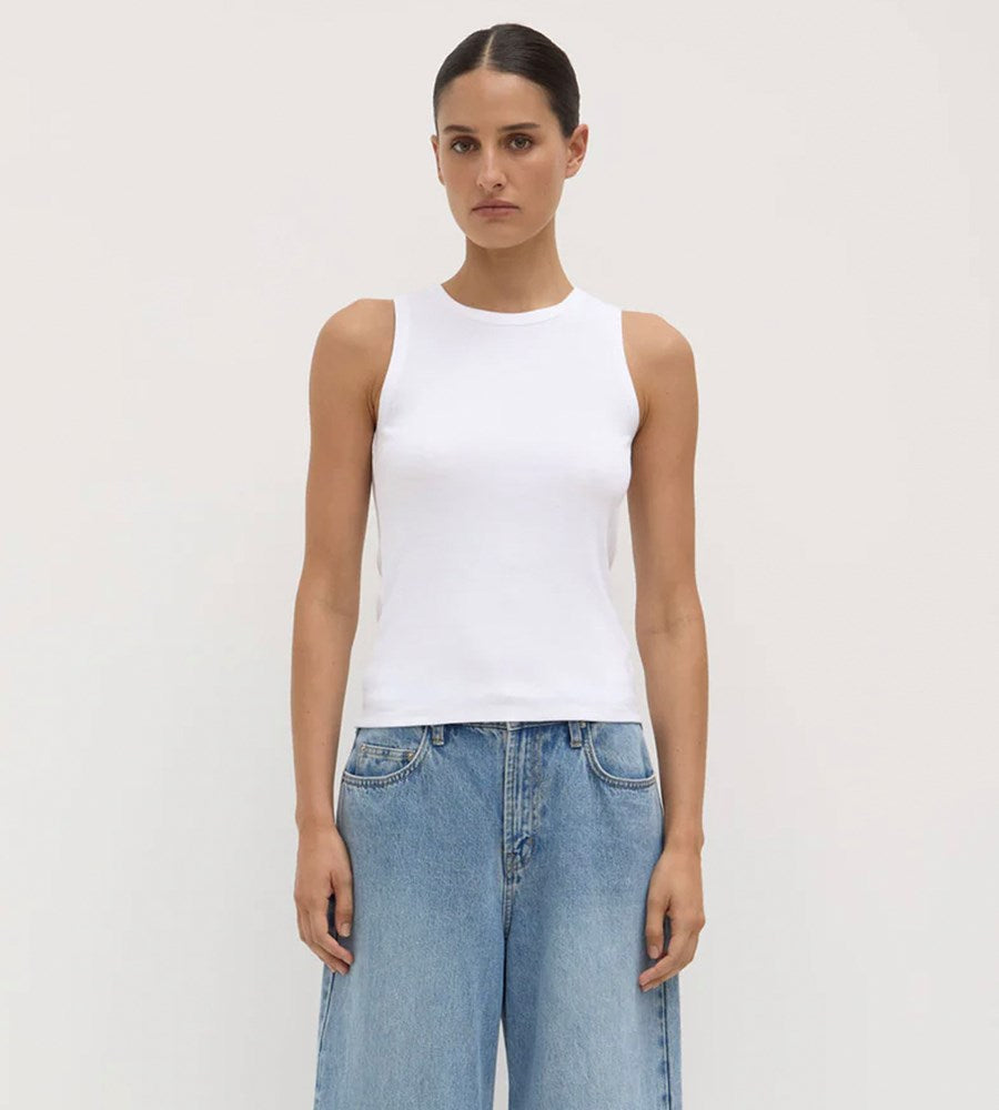 Person wearing a white sleeveless top and light blue jeans on a plain background