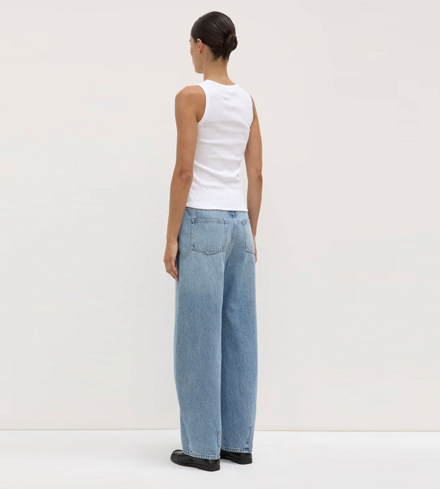 Person wearing a white sleeveless top and light blue jeans on a plain background