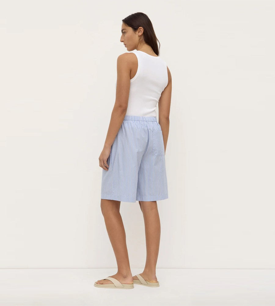 Woman wearing a white tank top and light blue striped shorts on a white background