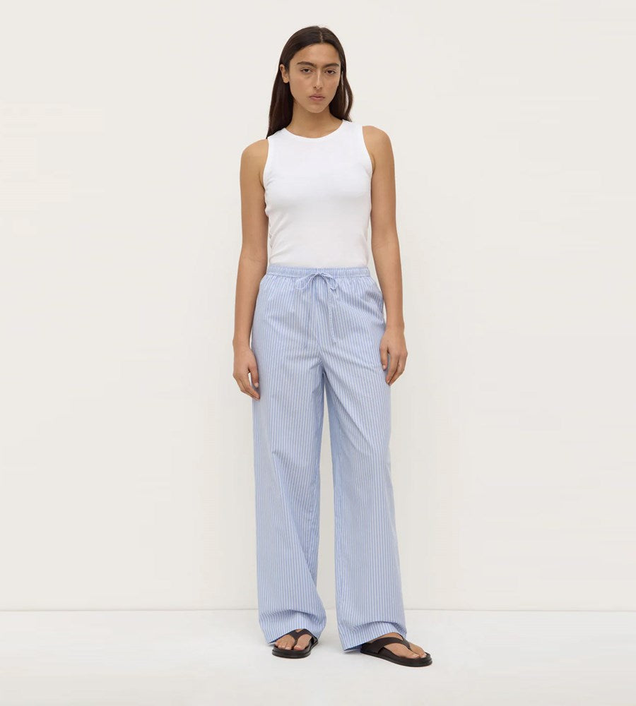 Woman wearing a white sleeveless top and light blue striped pants on a white background