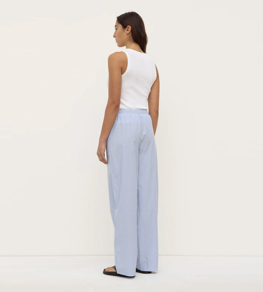 Woman wearing a white sleeveless top and light blue striped pants on a white background