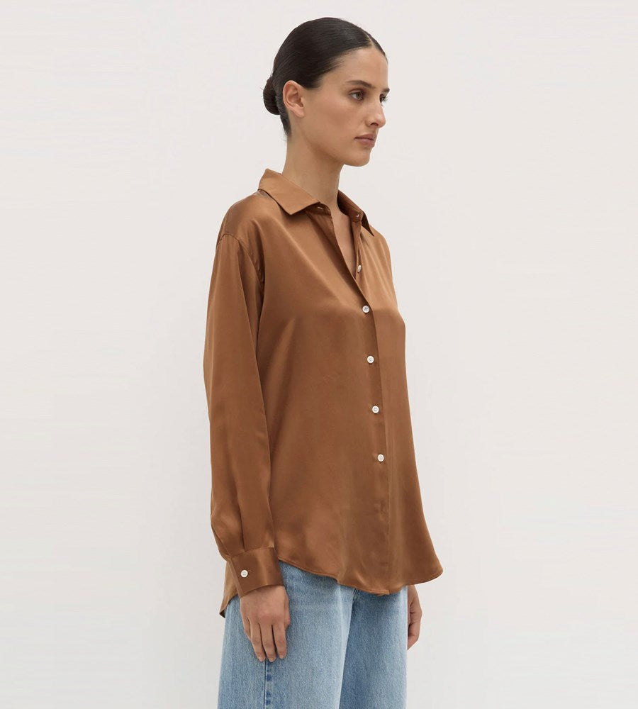Woman wearing a brown satin shirt and blue jeans on a white background