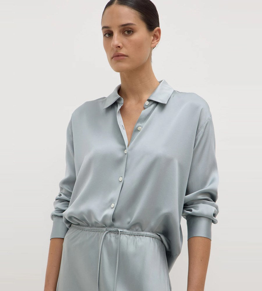Woman wearing a light gray shirt and pants on a plain background