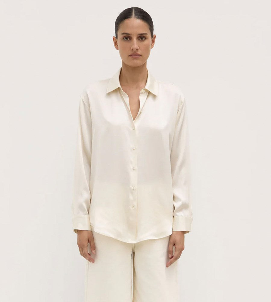 Woman wearing a cream-colored shirt and pants on a plain background