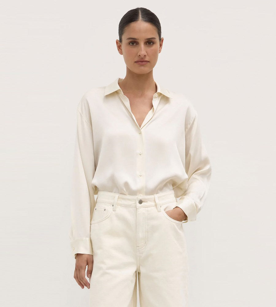 Woman wearing a white shirt and cream pants against a plain background