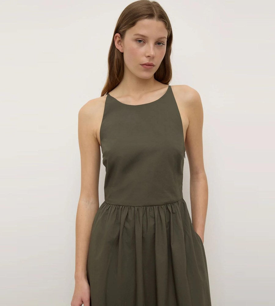 Woman wearing a green sleeveless dress against a plain background
