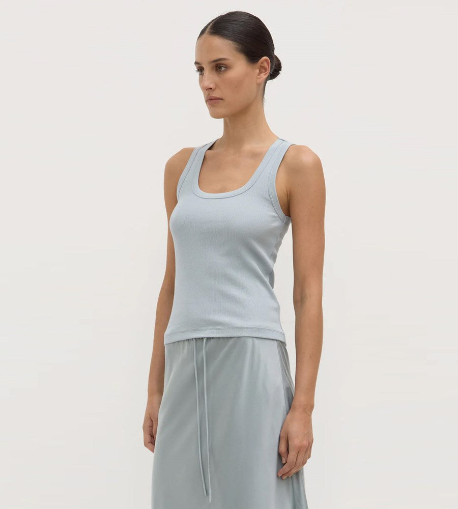 Woman wearing a light blue tank top and gray pants on a plain background