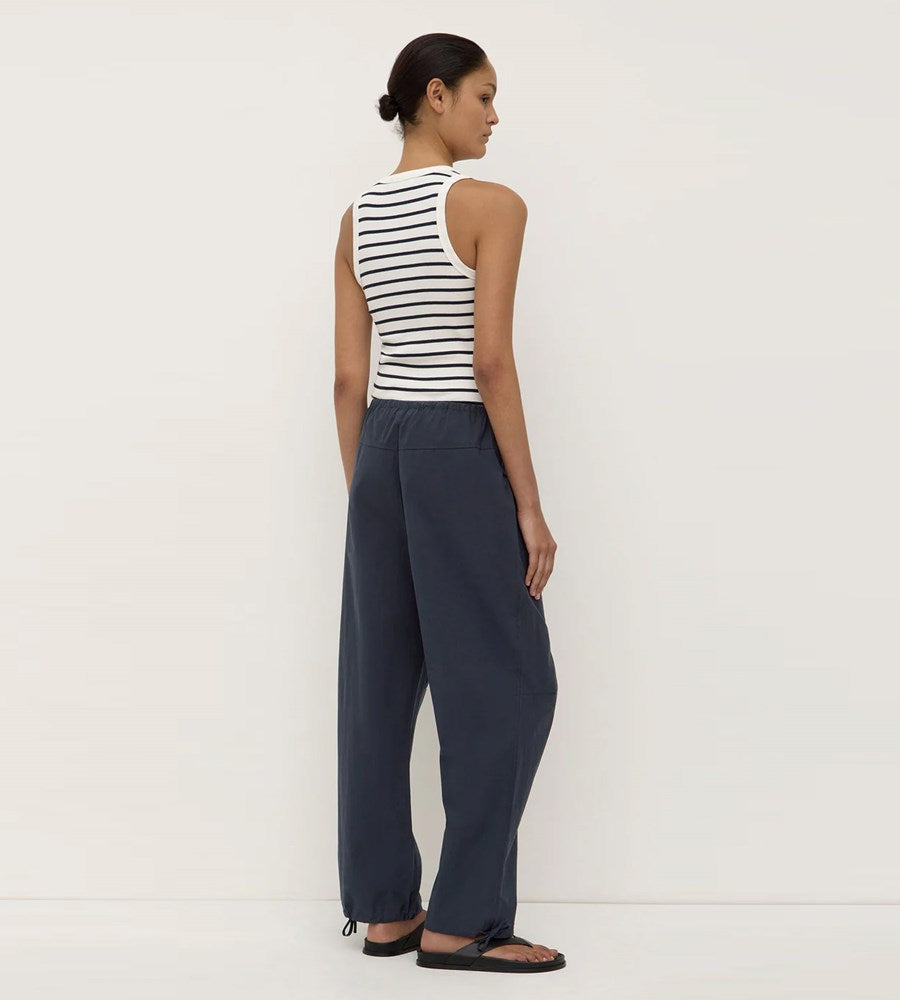 Woman wearing a striped tank top and dark pants against a white background