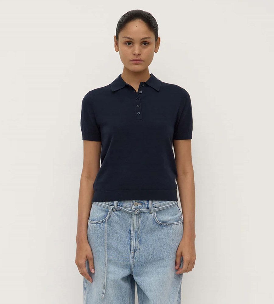 Person wearing a navy polo shirt and light blue jeans against a plain background