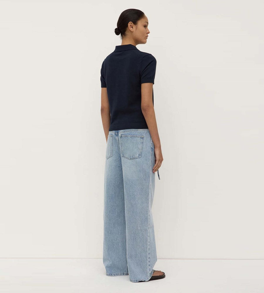 Person wearing a navy polo shirt and light blue jeans against a white background