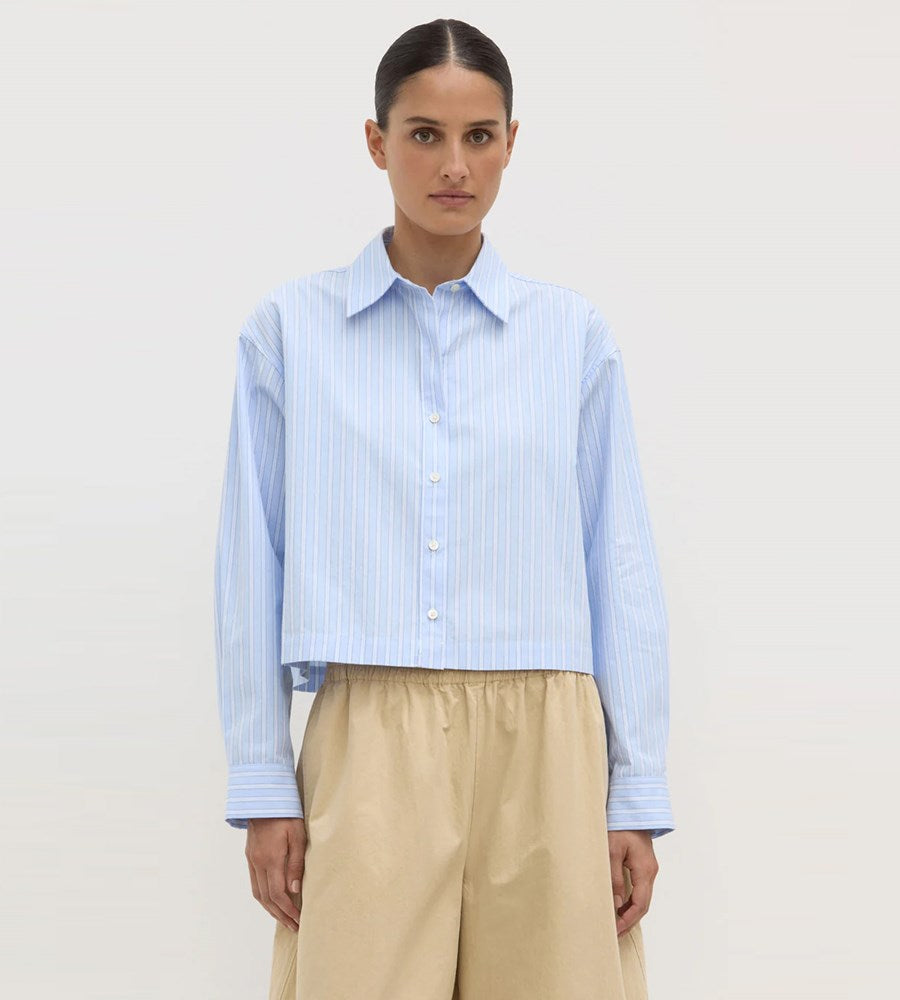 Woman wearing a light blue striped shirt and beige pants on a white background