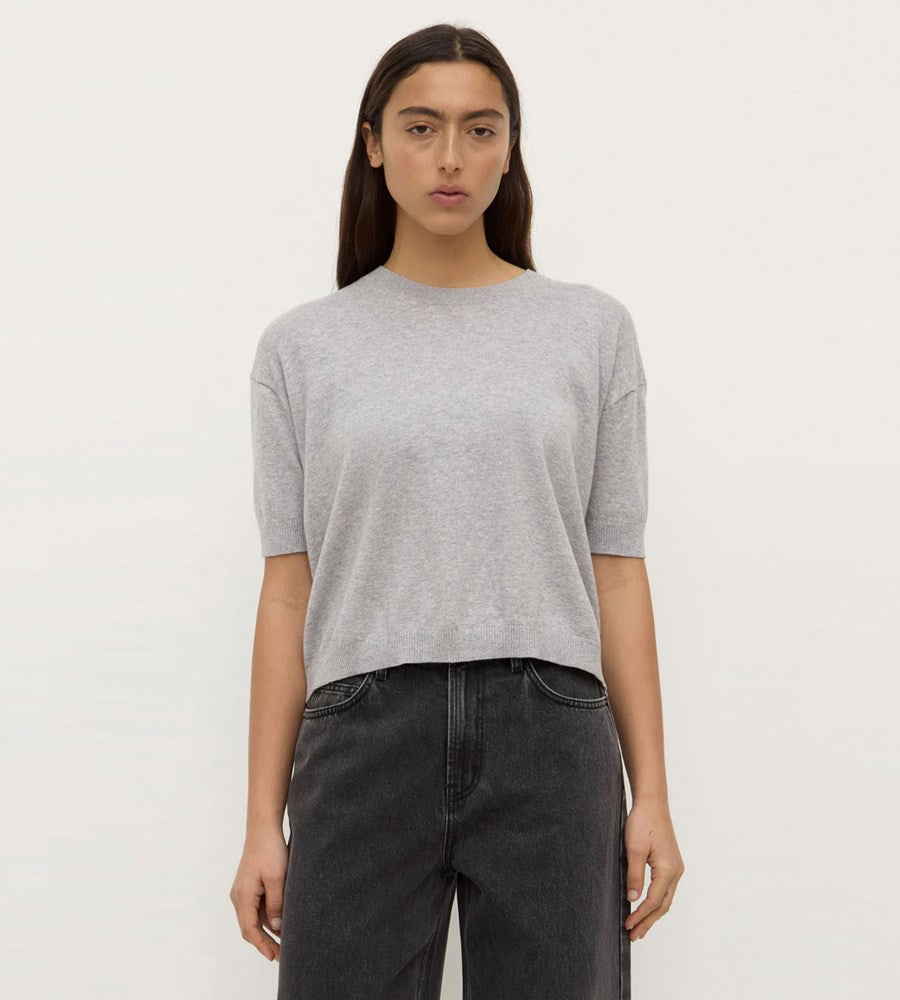 Person wearing a gray sweater and black pants on a white background