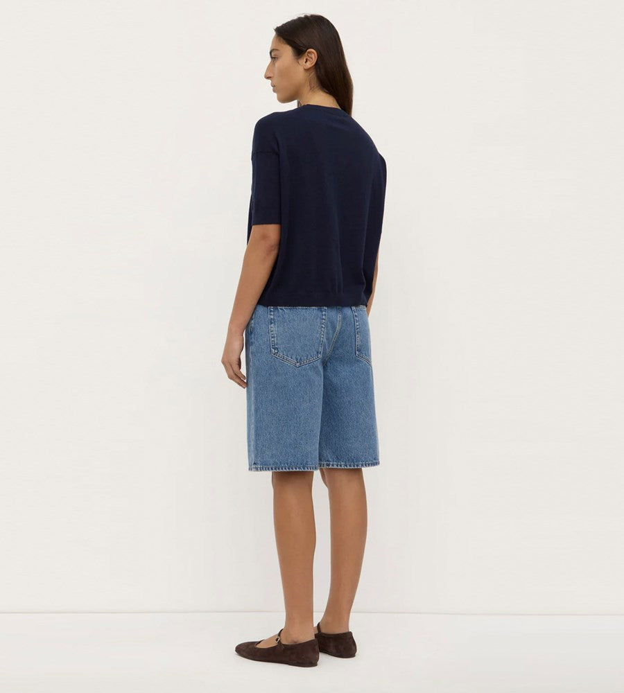 Woman wearing a navy blue top and denim shorts on a white background