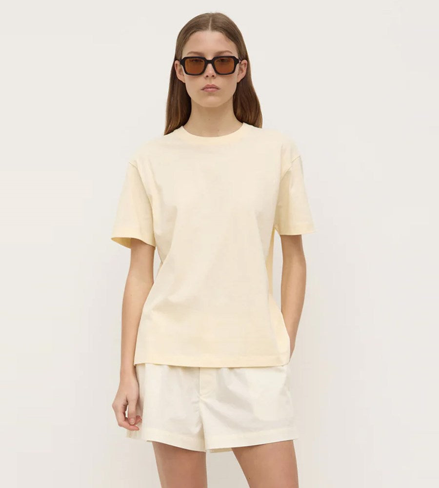 Person wearing a light yellow t-shirt and shorts with sunglasses on a white background