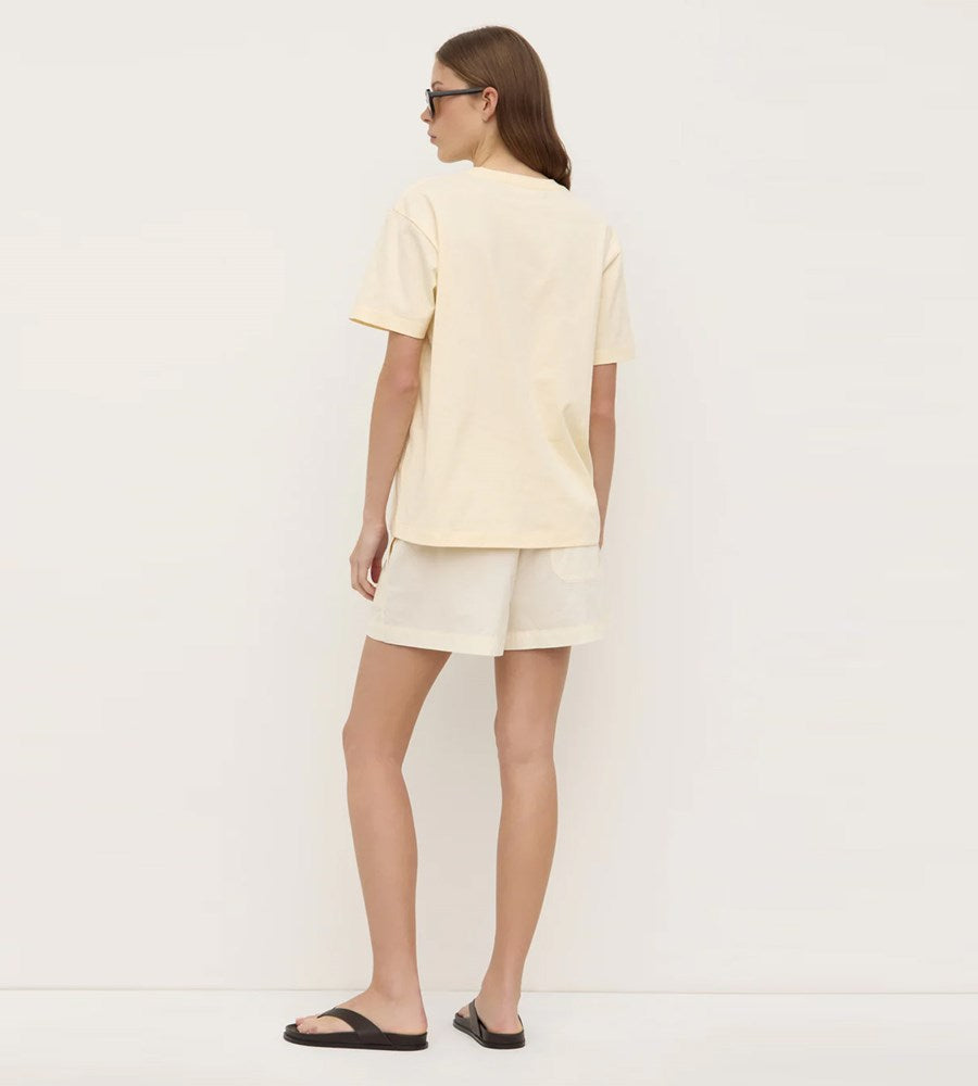 Woman wearing a light yellow t-shirt and shorts on a plain background