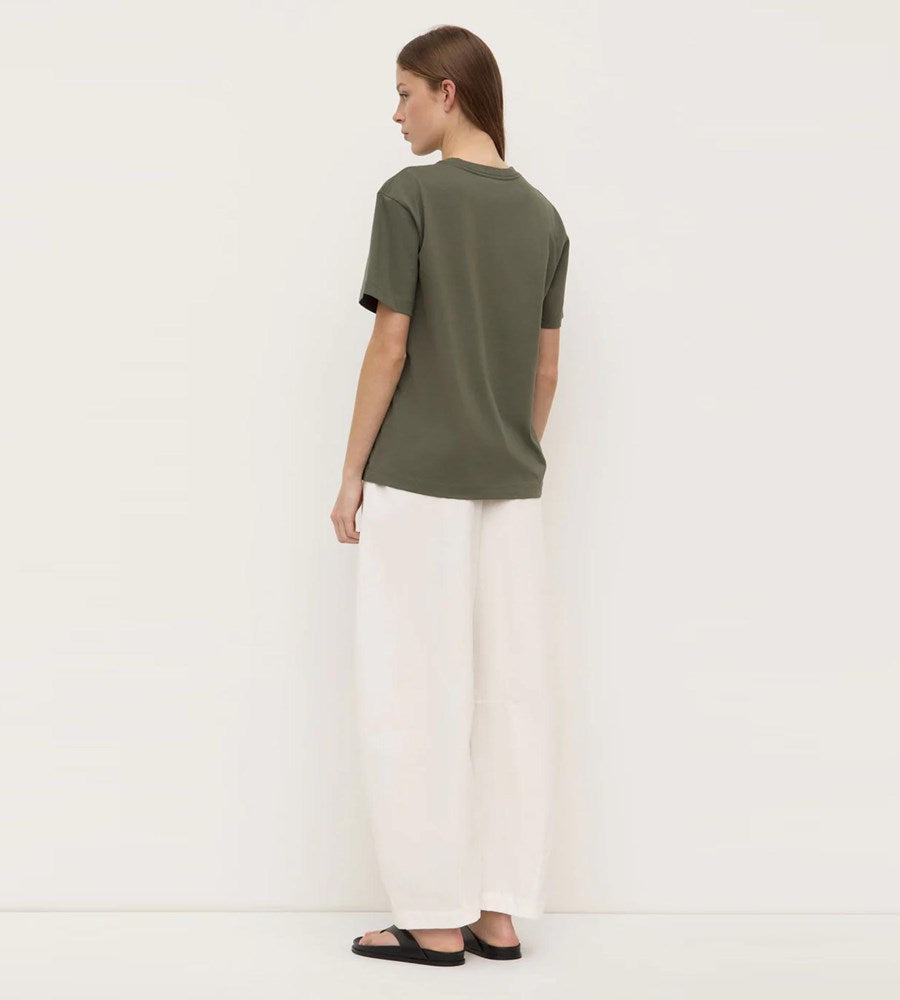 Person wearing a green t-shirt and white pants on a plain background