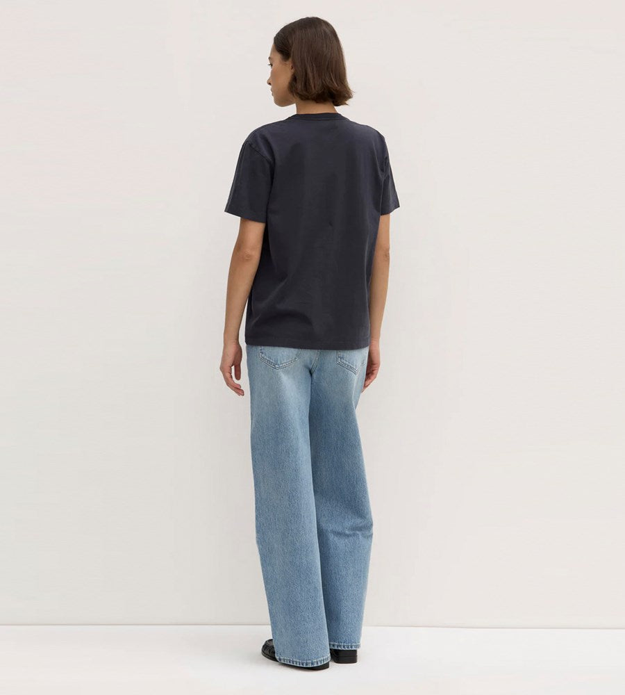Person wearing a black t-shirt and blue jeans standing against a white background
