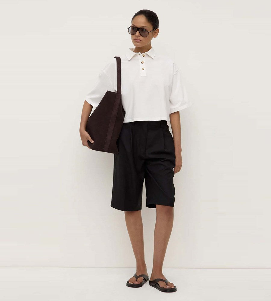 Person wearing a white shirt, black shorts, and holding a brown bag against a white background