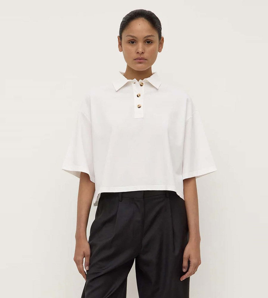 Person wearing a white blouse with a collar and black pants on a plain background