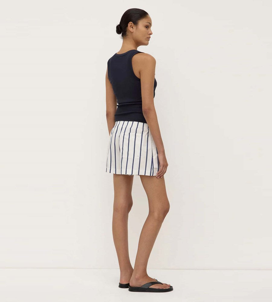 Woman wearing a black sleeveless top and white striped skirt on a white background