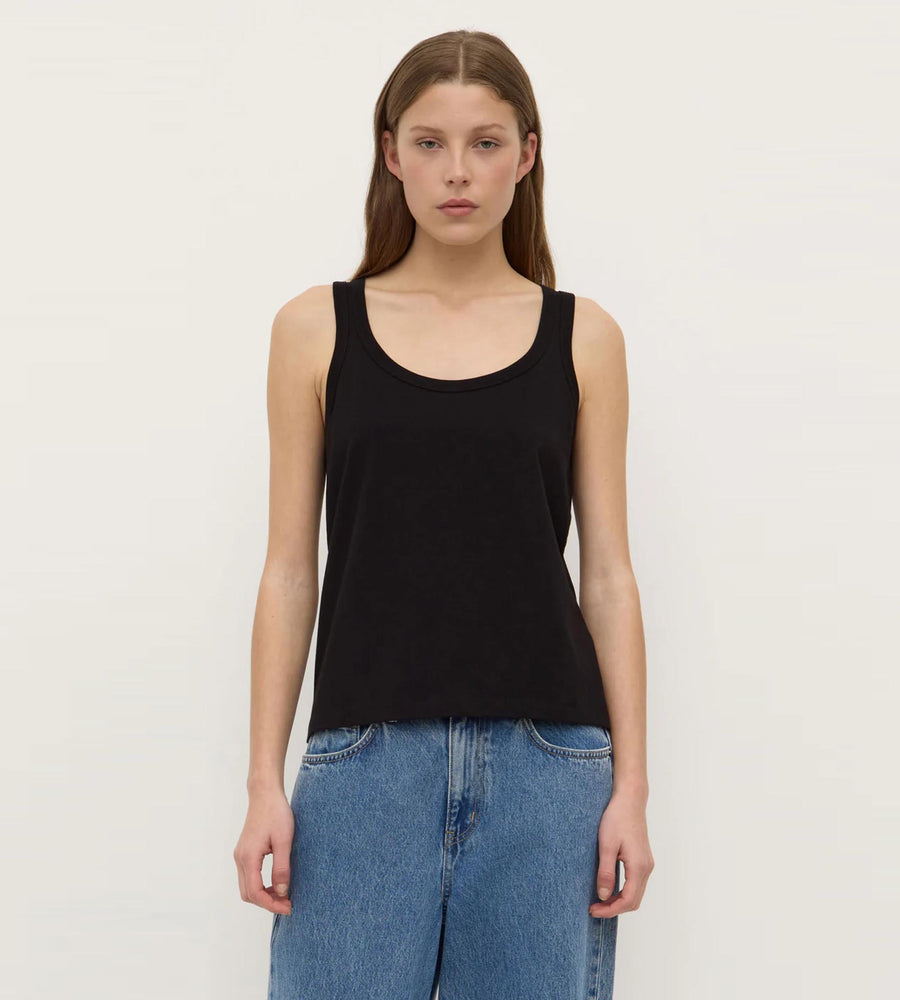 Person wearing a black tank top and blue jeans on a plain background