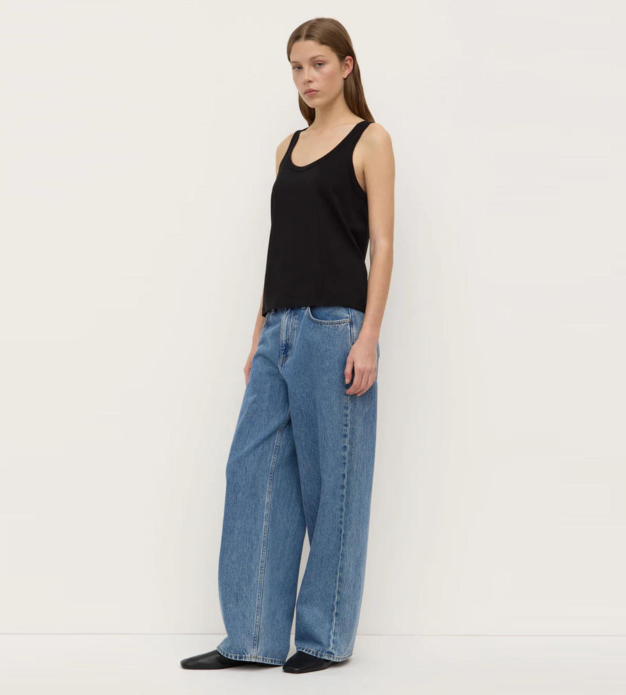 Woman wearing a black sleeveless top and blue jeans on a white background