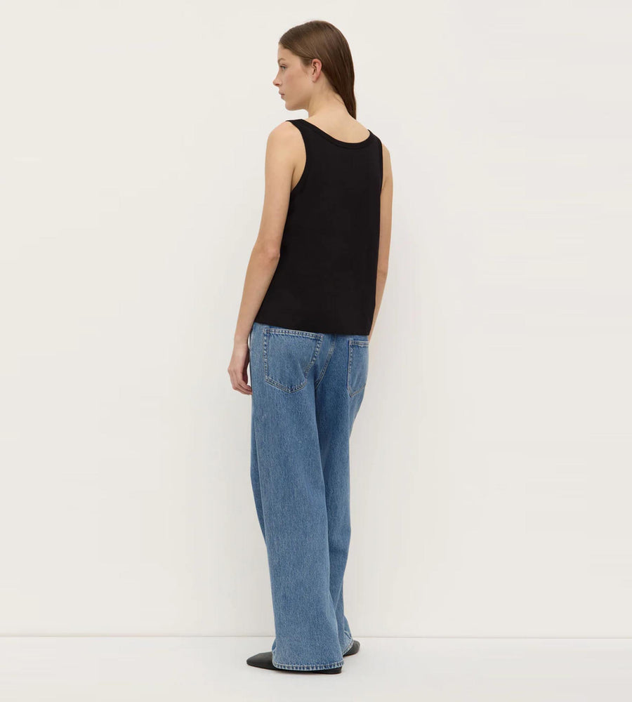 Person wearing a black sleeveless top and blue jeans against a white background