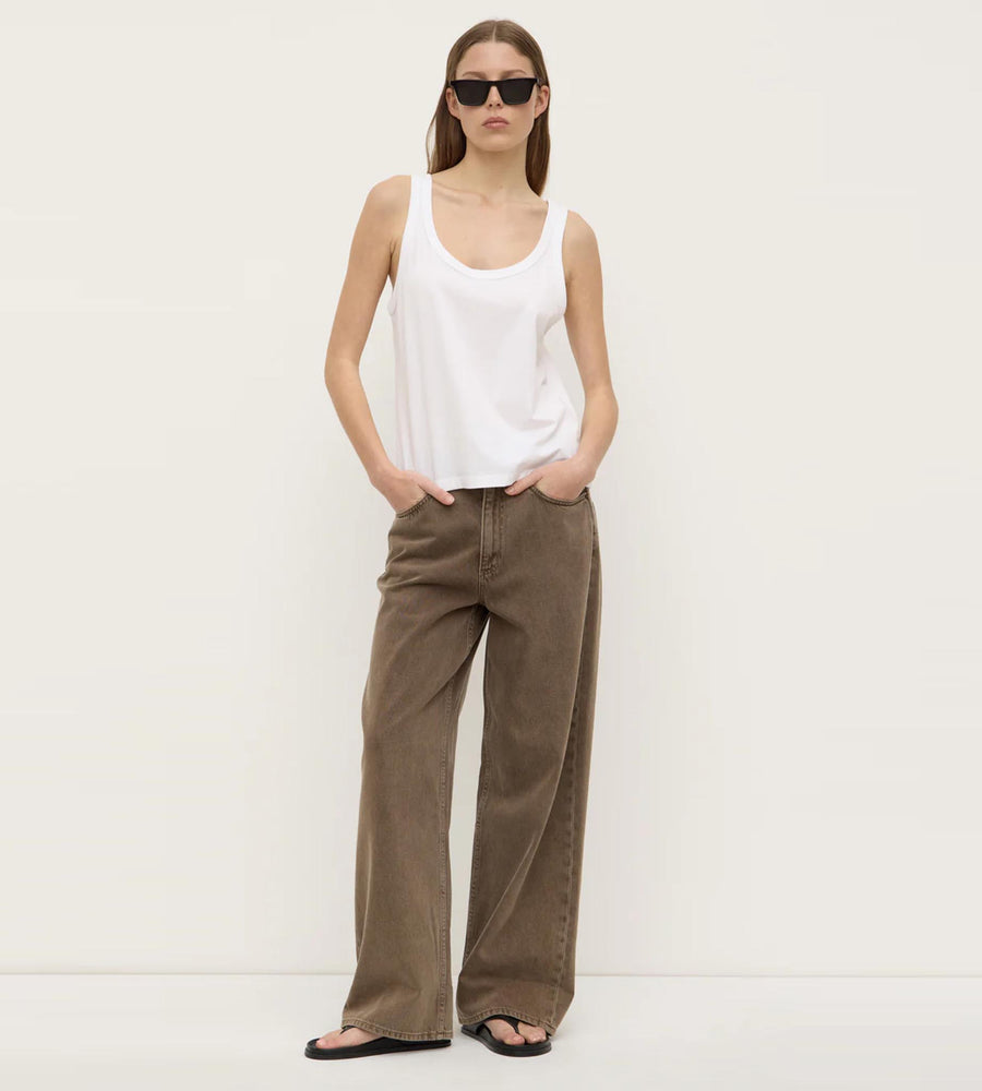 Woman wearing a white tank top and brown wide-leg pants against a white background