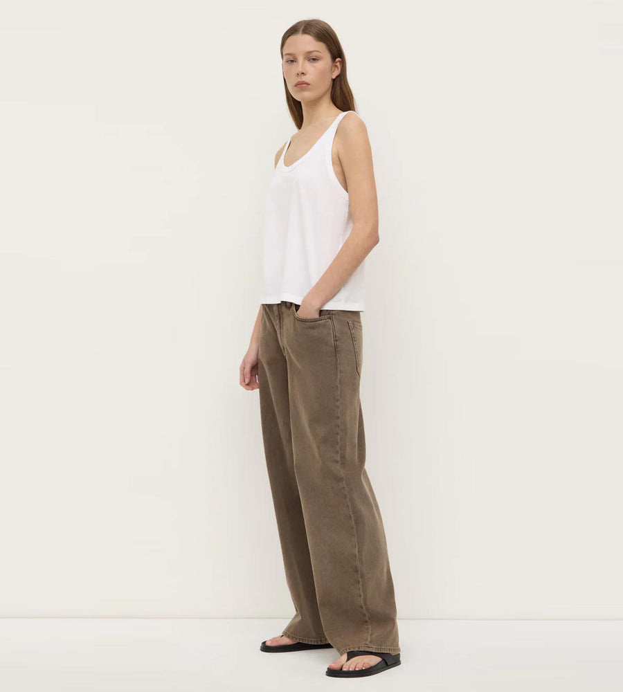 Woman wearing a white sleeveless top and brown pants against a white background